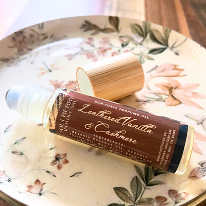 A bottle of Leathered Vanilla & Cashmere non-toxic perfume oil with its bamboo cap off, resting on a floral ceramic plate.